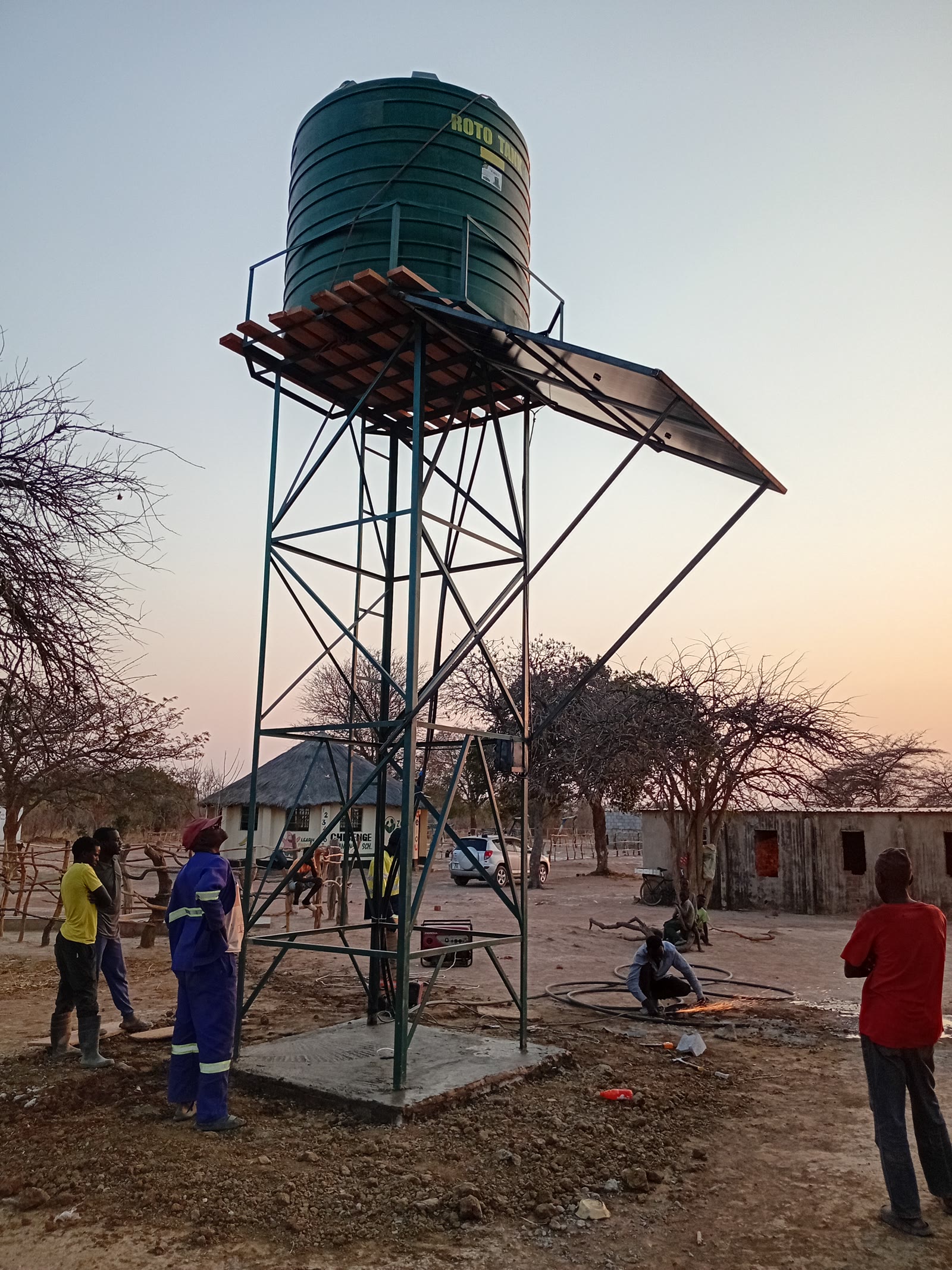 A water tower with a green tank standing over a village at dusk